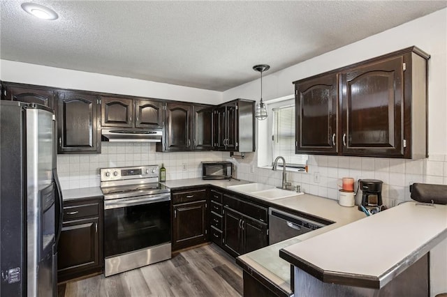 kitchen with hanging light fixtures, sink, kitchen peninsula, appliances with stainless steel finishes, and dark hardwood / wood-style floors