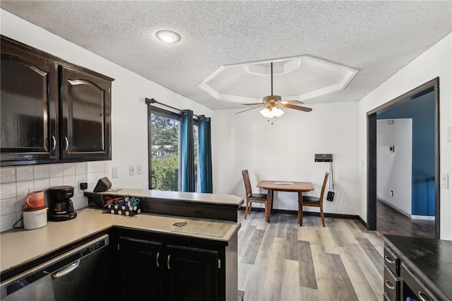 kitchen with ceiling fan, stainless steel dishwasher, a textured ceiling, light hardwood / wood-style flooring, and a tray ceiling