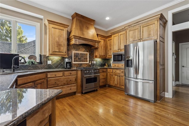 kitchen with a sink, appliances with stainless steel finishes, ornamental molding, and custom range hood