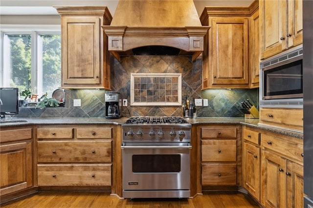 kitchen featuring brown cabinetry, custom range hood, wood finished floors, and stainless steel appliances