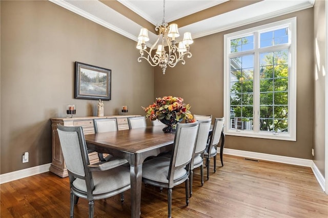 dining space featuring crown molding, a raised ceiling, an inviting chandelier, and light hardwood / wood-style flooring