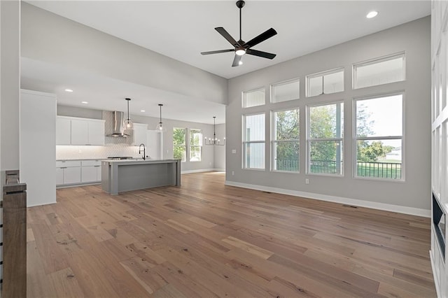 unfurnished living room featuring ceiling fan with notable chandelier, light wood-type flooring, and sink