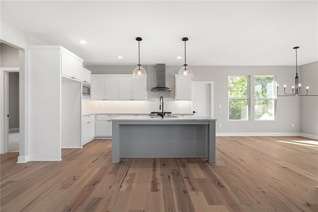 kitchen with light hardwood / wood-style floors, wall chimney exhaust hood, an island with sink, and white cabinets