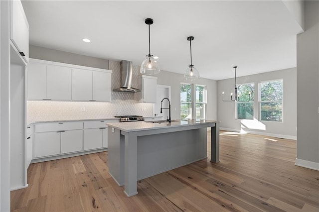 kitchen with wall chimney exhaust hood, white cabinetry, sink, and light hardwood / wood-style flooring