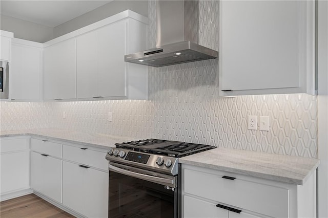 kitchen with light stone counters, white cabinets, gas range, wall chimney exhaust hood, and light hardwood / wood-style flooring