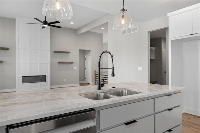 kitchen featuring light stone countertops, white cabinets, pendant lighting, and sink