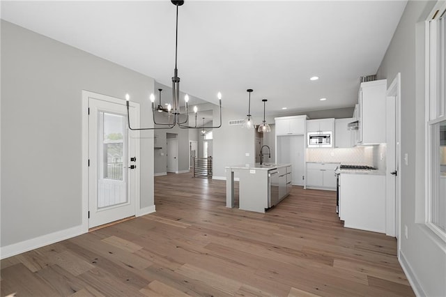 kitchen featuring light wood-type flooring, a kitchen island with sink, white cabinetry, hanging light fixtures, and stainless steel appliances