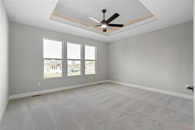 spare room featuring light carpet, a tray ceiling, and ceiling fan