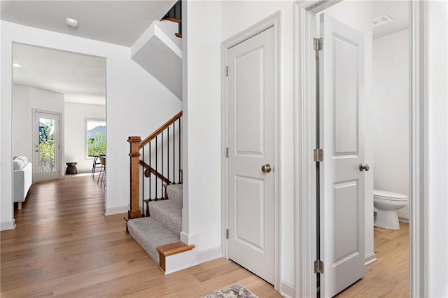 corridor featuring visible vents, light wood-style flooring, baseboards, and stairs