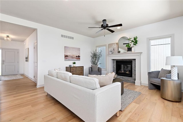 living room with light wood-style flooring, visible vents, baseboards, a ceiling fan, and a glass covered fireplace