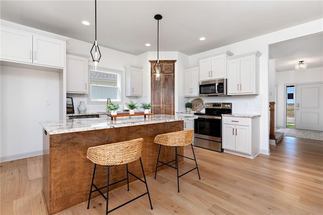 kitchen with light wood finished floors, tasteful backsplash, a kitchen island, stainless steel appliances, and white cabinetry