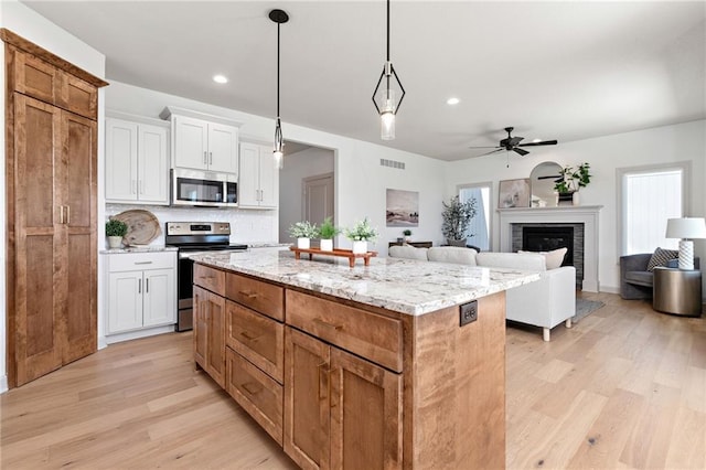 kitchen with appliances with stainless steel finishes, a kitchen island, a glass covered fireplace, and light wood-style flooring