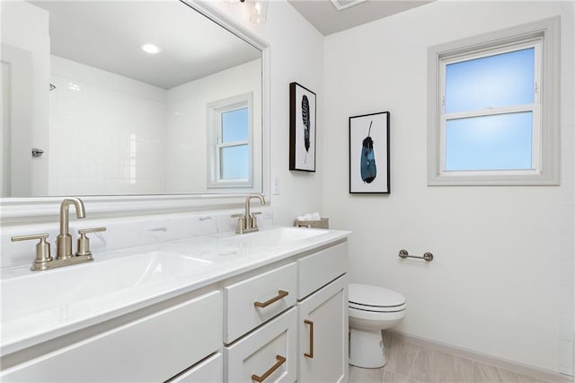 bathroom with toilet, double vanity, walk in shower, and a sink