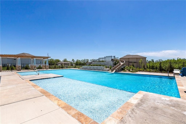 community pool with a water slide, a patio area, and fence