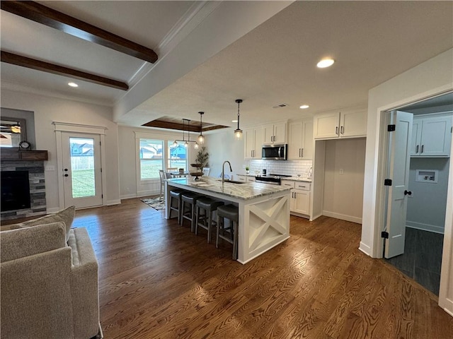 kitchen featuring decorative light fixtures, white cabinetry, sink, light stone counters, and a center island with sink