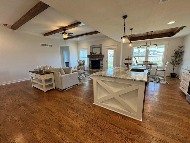 kitchen featuring pendant lighting, white cabinetry, a kitchen island with sink, dark hardwood / wood-style floors, and light stone countertops