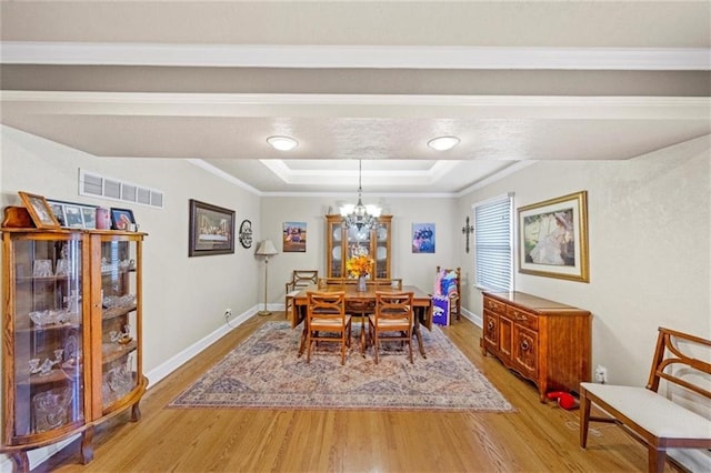 dining area with a tray ceiling, ornamental molding, light hardwood / wood-style flooring, and a chandelier