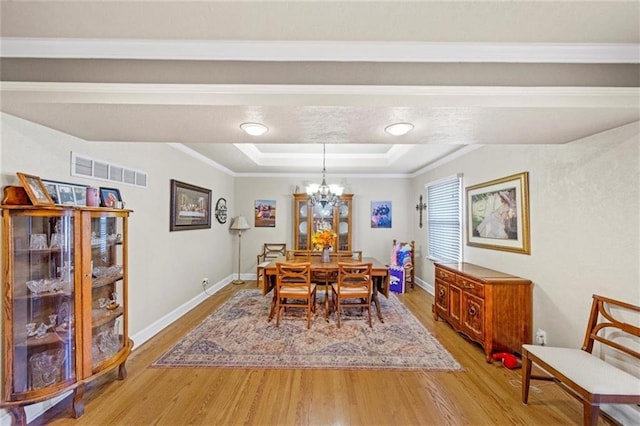 dining area with visible vents, light wood finished floors, an inviting chandelier, ornamental molding, and a tray ceiling