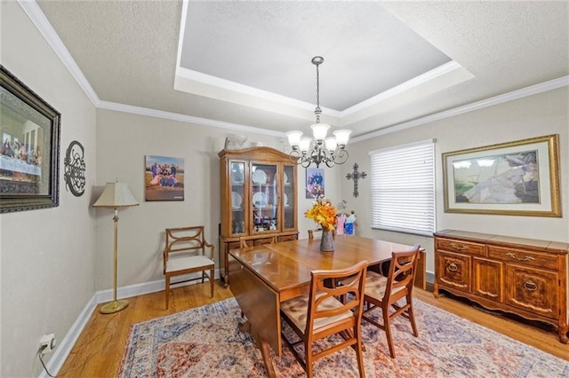 dining area with a raised ceiling, a textured ceiling, a chandelier, light hardwood / wood-style flooring, and ornamental molding