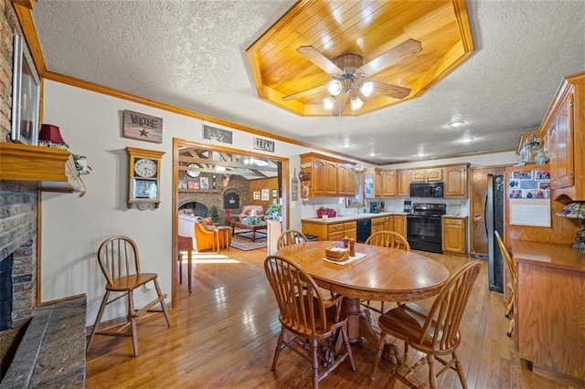 dining space featuring a fireplace with raised hearth, a textured ceiling, ceiling fan, and light wood finished floors