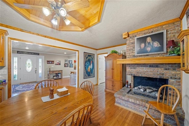 dining area with ceiling fan, a fireplace, a textured ceiling, light wood-style flooring, and baseboards