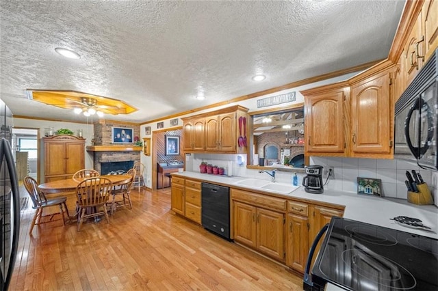 kitchen with light countertops, a textured ceiling, a large fireplace, a sink, and black appliances