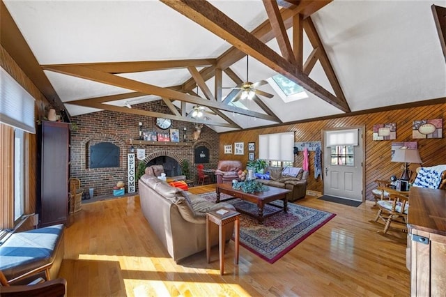 living area with ceiling fan, brick wall, a brick fireplace, lofted ceiling with skylight, and light wood-style flooring