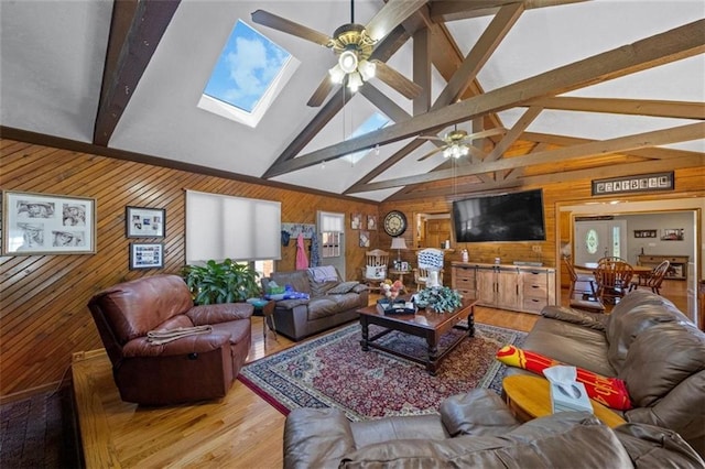 living room featuring a ceiling fan, wood walls, wood finished floors, and lofted ceiling with skylight