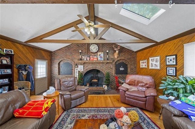 living room featuring wood walls, a ceiling fan, wood finished floors, and vaulted ceiling with skylight