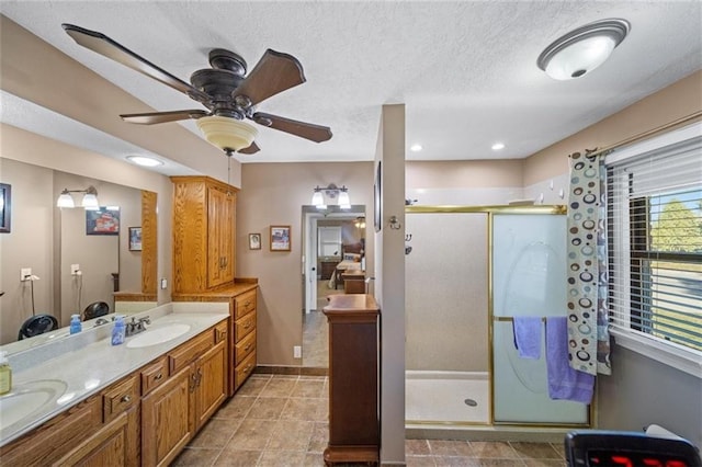ensuite bathroom with double vanity, ceiling fan, a textured ceiling, a sink, and a stall shower