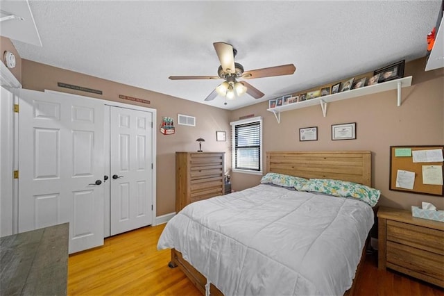bedroom featuring ceiling fan, a textured ceiling, wood finished floors, visible vents, and a closet