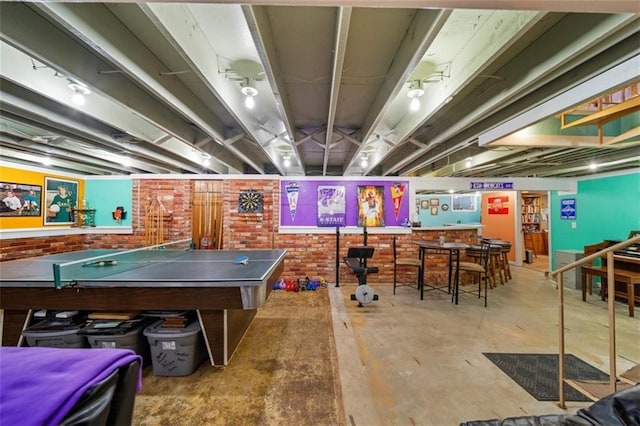 game room with unfinished concrete flooring and brick wall