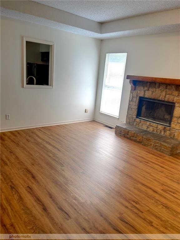 unfurnished living room with a textured ceiling, a stone fireplace, and hardwood / wood-style flooring