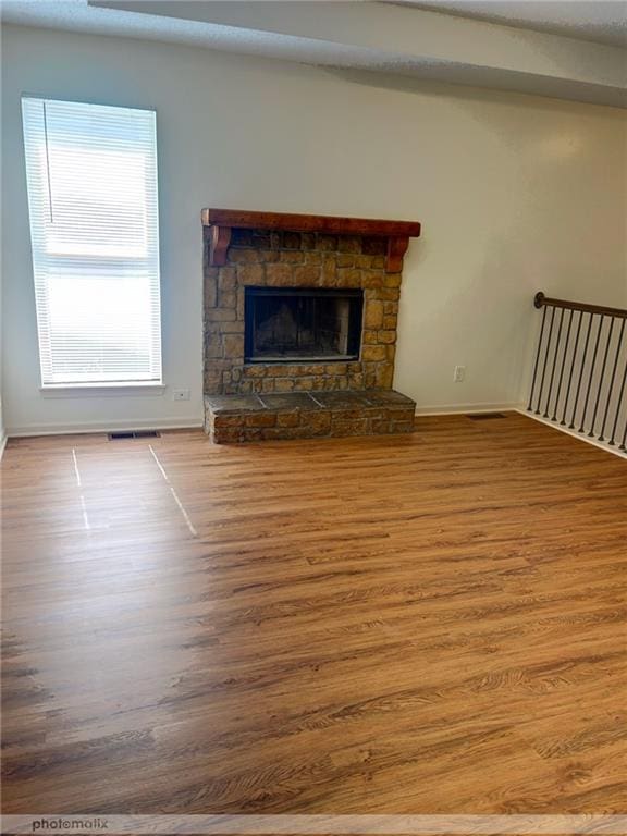 unfurnished living room with hardwood / wood-style floors and a stone fireplace