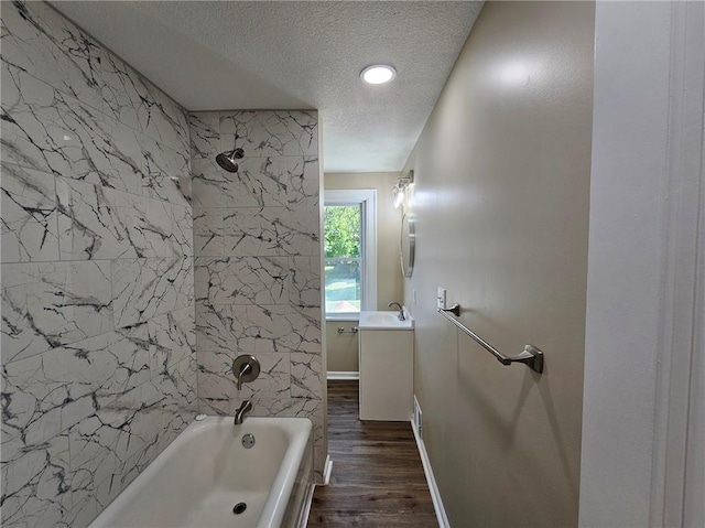 bathroom with wood-type flooring, a textured ceiling, tiled shower / bath combo, and vanity