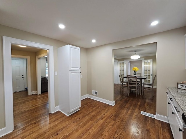 interior space featuring white cabinets, light stone counters, crown molding, and dark hardwood / wood-style flooring