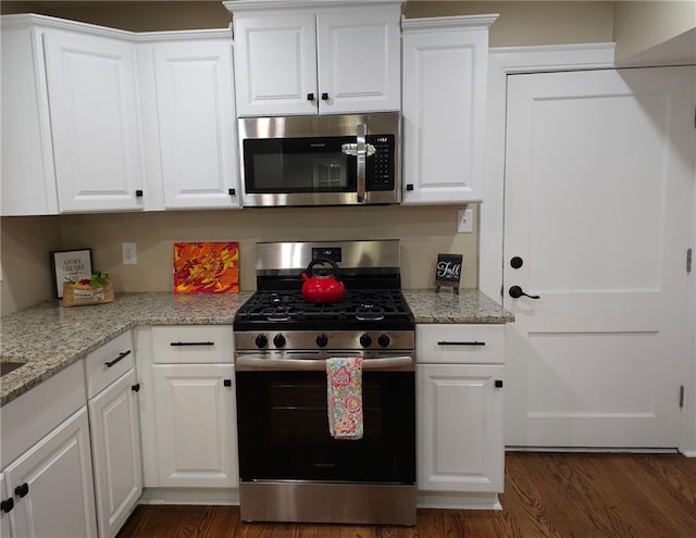 kitchen with light stone counters, white cabinets, appliances with stainless steel finishes, and dark hardwood / wood-style floors