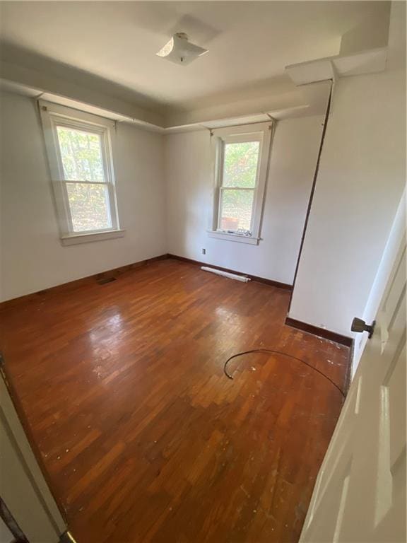 empty room with a wealth of natural light and dark hardwood / wood-style flooring