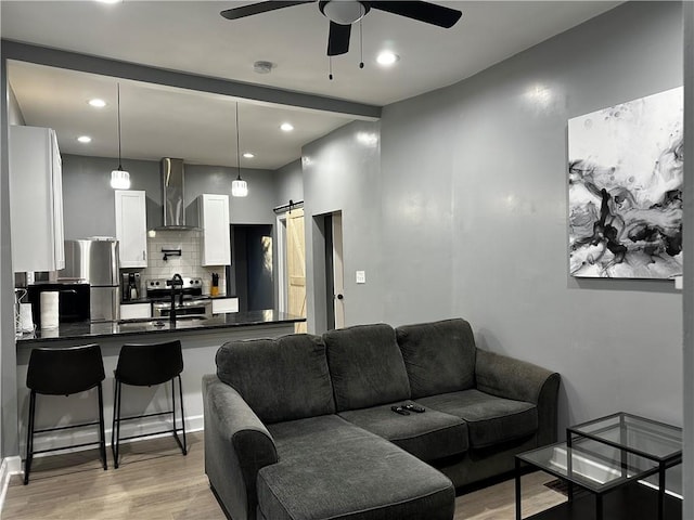 living room featuring ceiling fan, light hardwood / wood-style flooring, and a barn door