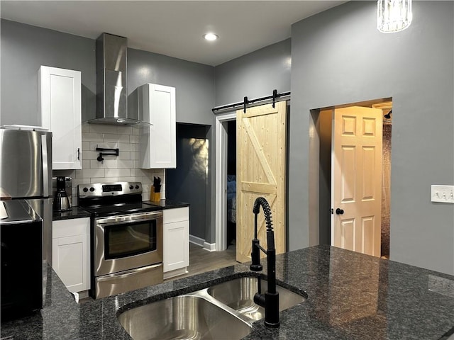 kitchen featuring stainless steel appliances, white cabinetry, wall chimney range hood, and a barn door