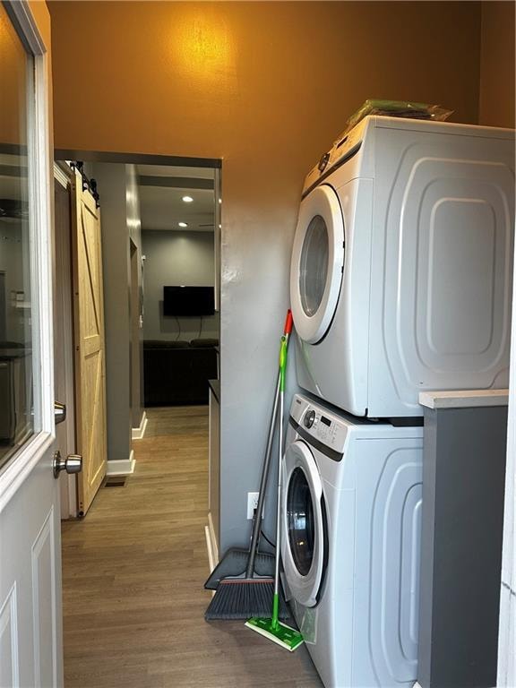 laundry area featuring a barn door, light hardwood / wood-style flooring, and stacked washer / drying machine