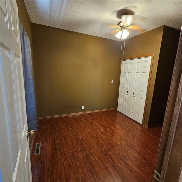 unfurnished bedroom with a textured ceiling, dark wood-type flooring, ceiling fan, and a closet