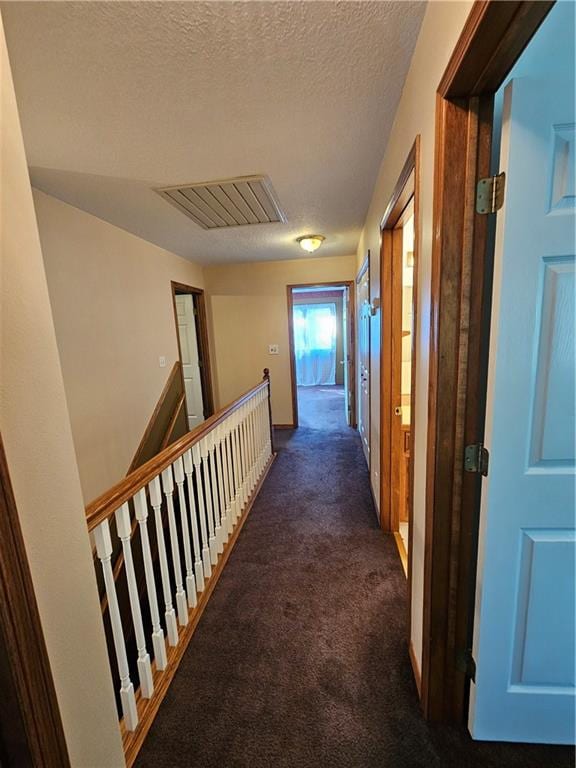 hall featuring a textured ceiling and dark colored carpet