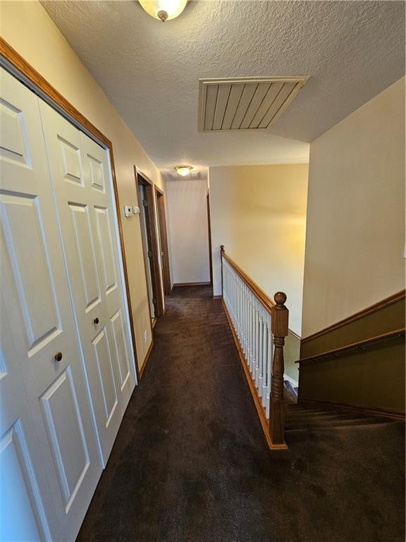 hallway featuring dark carpet and a textured ceiling