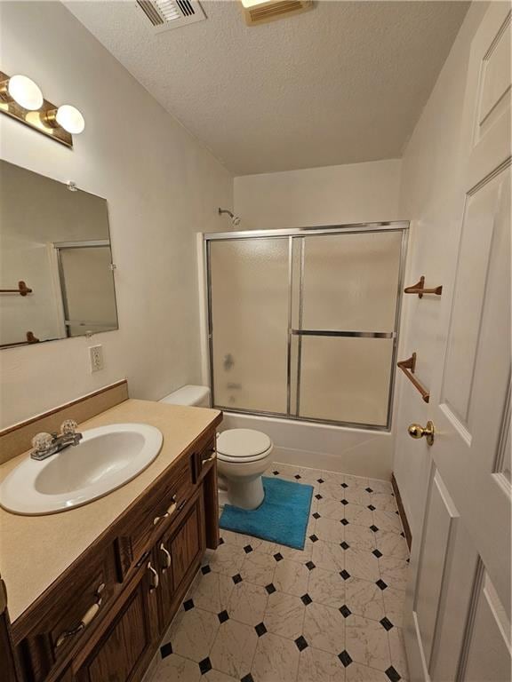 full bathroom with a textured ceiling, bath / shower combo with glass door, vanity, and toilet