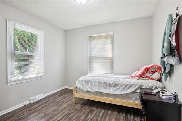 bedroom with multiple windows, a textured ceiling, and dark wood-type flooring