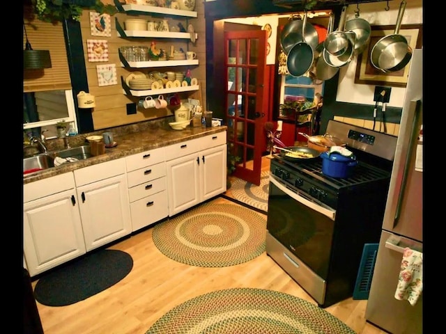 kitchen with light wood-type flooring, stainless steel gas stove, white cabinetry, and sink