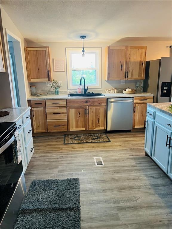 kitchen with pendant lighting, light wood-type flooring, appliances with stainless steel finishes, and sink