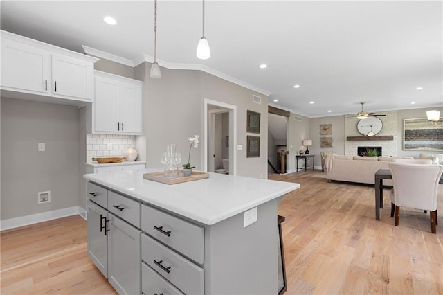 kitchen featuring white cabinetry, a center island, a large fireplace, decorative backsplash, and decorative light fixtures