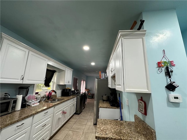 kitchen featuring appliances with stainless steel finishes, dark stone countertops, light tile patterned flooring, white cabinets, and sink